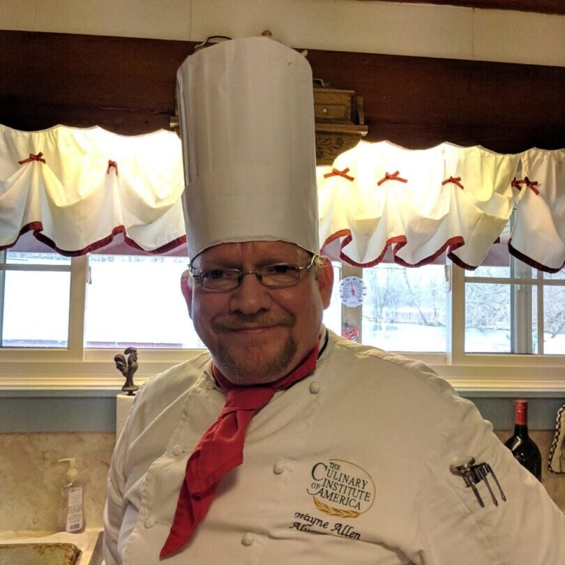 A man in chef 's outfit standing next to sink.